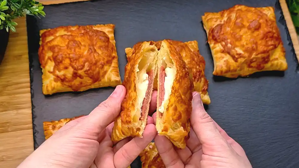 Detailansicht einer aufgeschnittenen Blätterteig-Tasche mit Fokus auf den flüssigen Schmelzkäse-Kern, die würzigen Salamischichten und die goldgelbe Käsekruste.