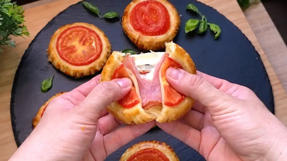 Detailansicht einer aufgeschnittenen, runden Blätterteigtasche mit Fokus auf den geschmolzenen Käse, saftigen Schinken, Kräuterfrischkäse und die krosse Kruste.
