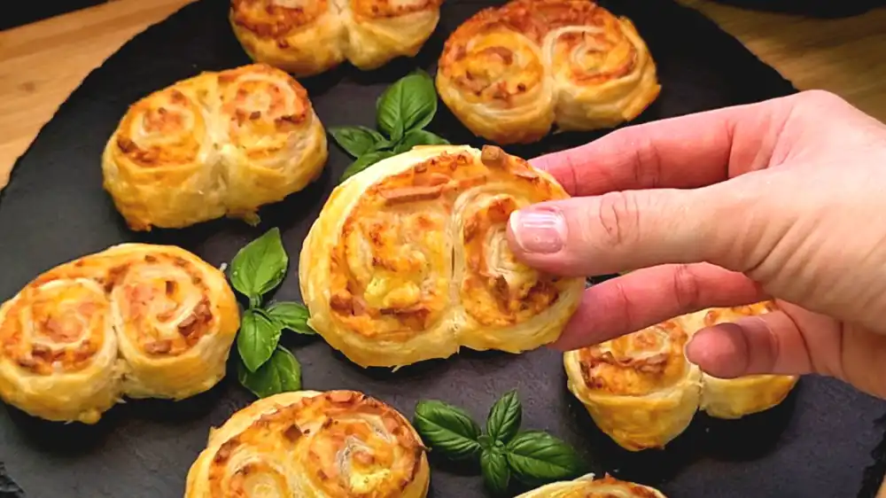 Detailansicht eines gebackenen Schinken-Käse-Öhrchens mit Fokus auf die knusprigen Blätterteigschichten und den herausgebackenen, krossen Käserand.