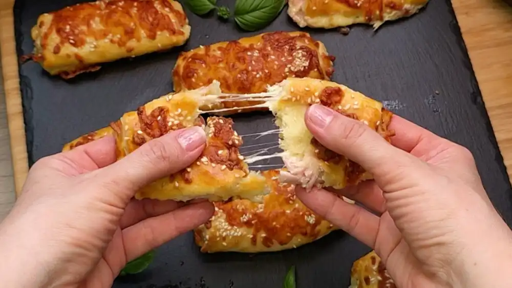 Detailansicht eines frisch gebackenen Schinken-Käse-Stäbchens aus Blätterteig mit Fokus auf den geschmolzenen Käserand, die saftige Schinkenfüllung und die gerösteten Sesamsamen.