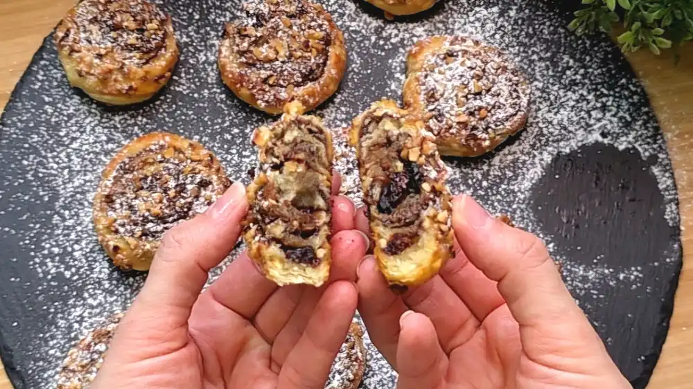Detailansicht einer frisch gebackenen Blätterteig-Schnecke mit Fokus auf die geschmolzene Schokocreme, die roten Preiselbeeren und die gerösteten Haselnussstücke.