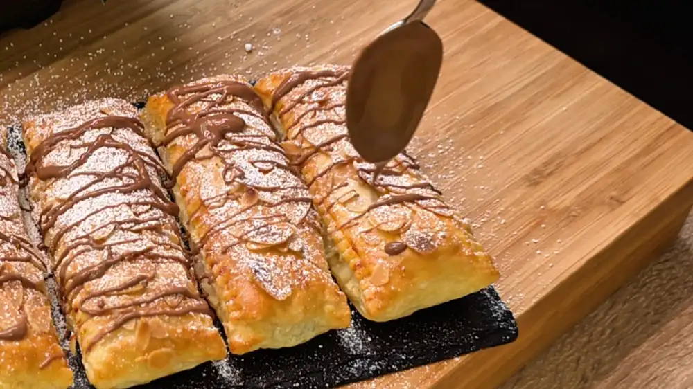 Detailansicht eines aufgeschnittenen Blätterteig-Riegels mit Fokus auf die saftige weiße Quarkcreme, geschmolzene Schokoladenstücke und kross geröstete Mandeln am Rand.