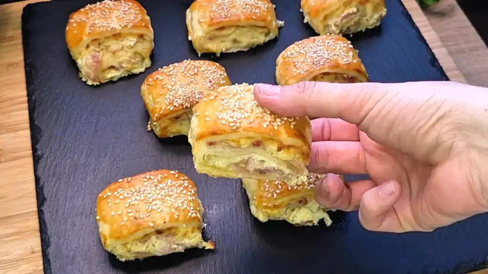 Detailansicht einer frisch gebackenen Speck-Käse-Rolle aus Blätterteig mit Fokus auf den geschmolzenen Käserand, die Kräuterfüllung und die gerösteten Sesamsamen.
