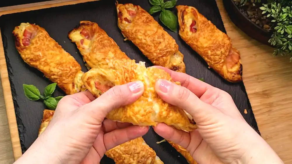 Detailansicht einer aufgeschnittenen Blätterteigtasche mit Fokus auf den knusprig gebratenen Speck, die cremige Kräuterfrischkäse-Füllung und den geschmolzenen Käse.