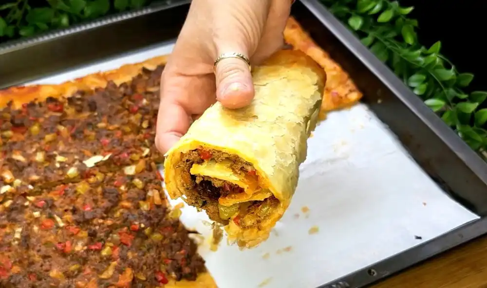 Detailansicht eines frisch gebackenen Blätterteig-Lahmacun mit Fokus auf die saftige Hackfleischschicht, die roten Paprikastücke und den blättrig-krossen Rand.