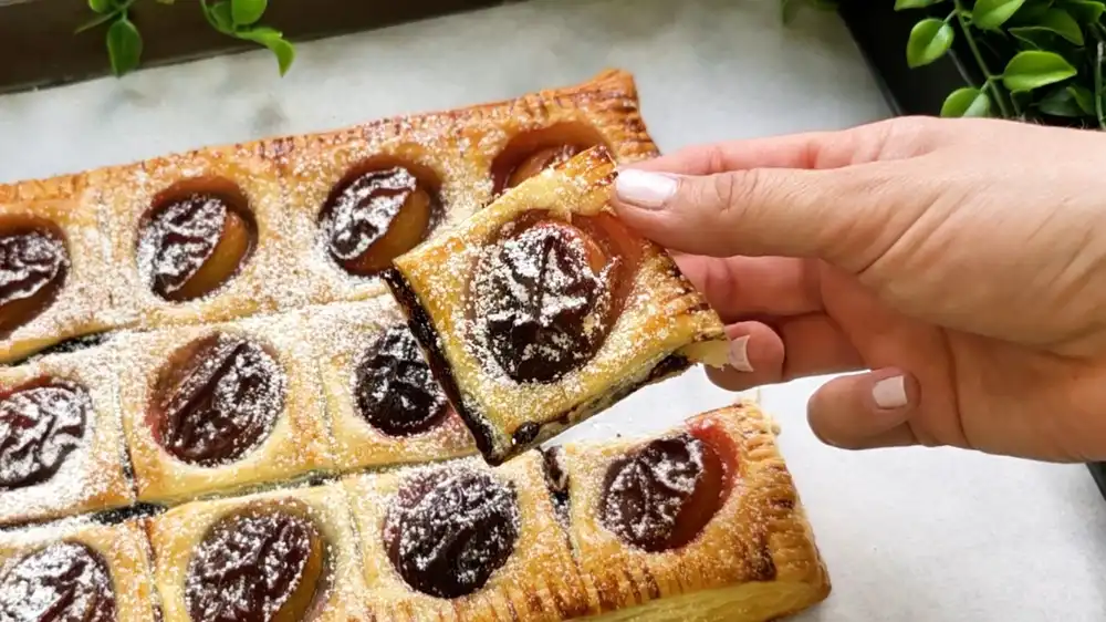 Makroaufnahme von einem Zwetschgen-Häppchen aus Blätterteig mit Fokus auf die zimtige Grieß-Zucker-Kruste und den saftigen Fruchtkern.