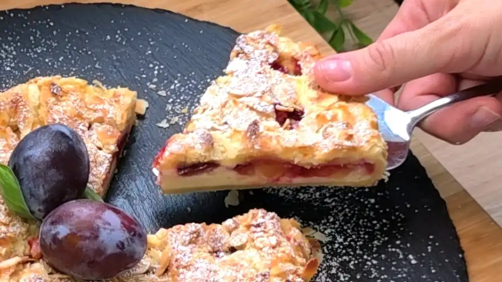 Detailansicht eines Kuchenschnitts mit Fokus auf die saftige Quark-Vanille-Schicht, die weichen Zwetschgenstücke und die gerösteten Mandelblättchen auf dem krossen Teiggitter.