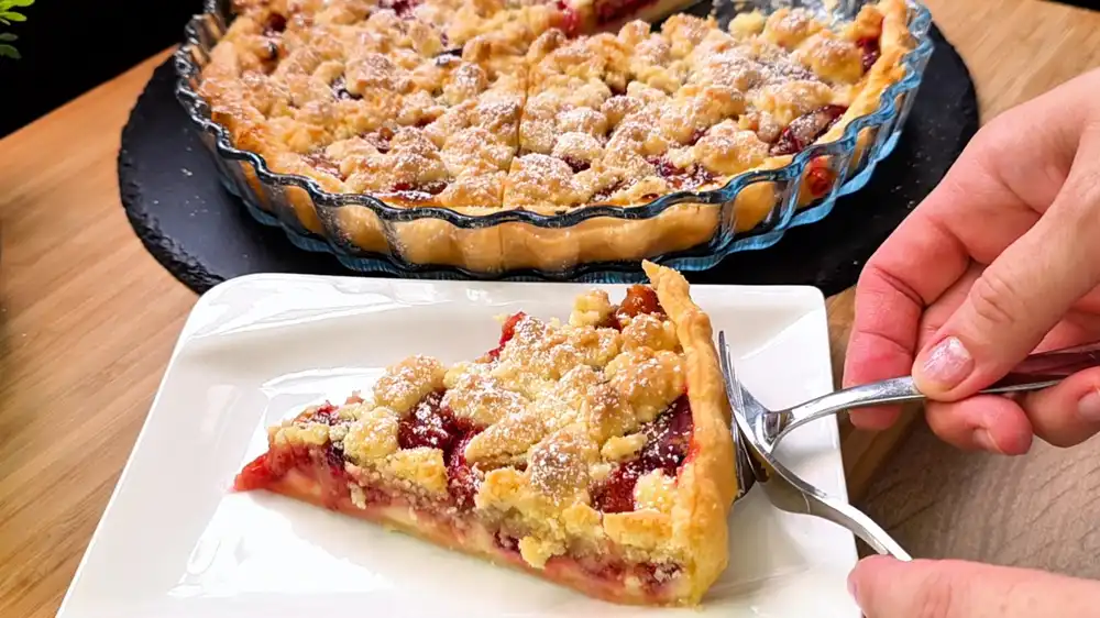 Detailansicht eines Kuchenschnitts mit Fokus auf den krossen Blätterteigboden, die cremige Quark-Schicht, saftige Pflaumen und dicke, goldgelbe Butterstreusel.