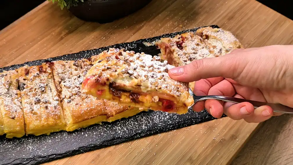Detailansicht des angeschnittenen Blätterteigstrudels, die die dicke Vanillepudding-Schicht, saftige lila Zwetschgenstücke und geschmolzene Schokoladentropfen zeigt.