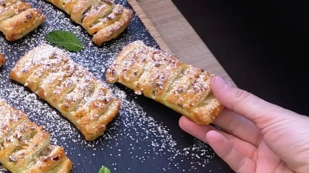 Detailansicht einer aufgeschnittenen Blätterteigtasche mit Fokus auf die warme, weiche Bananenschicht und die herauslaufenden Milchschokoladentropfen.