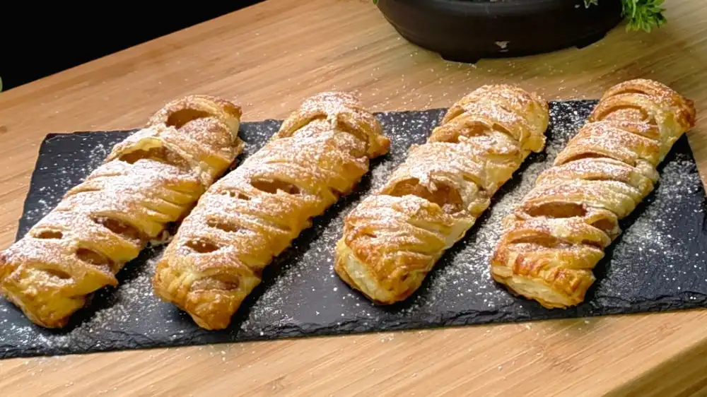 Eine stilvolle Etagere voller goldbraun gebackener Blätterteig-Vanille-Zimt-Rollen, fein mit Puderzucker bestäubt auf einer sommerlichen Kaffeetafel.