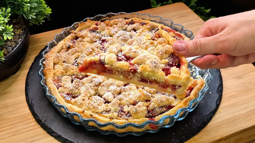 Ein herrlicher Zwetschgen-Quark-Streuselkuchen aus Blätterteig in einer 26 cm Springform, reichlich mit Puderzucker bestäubt auf einem sommerlichen Gartentisch.