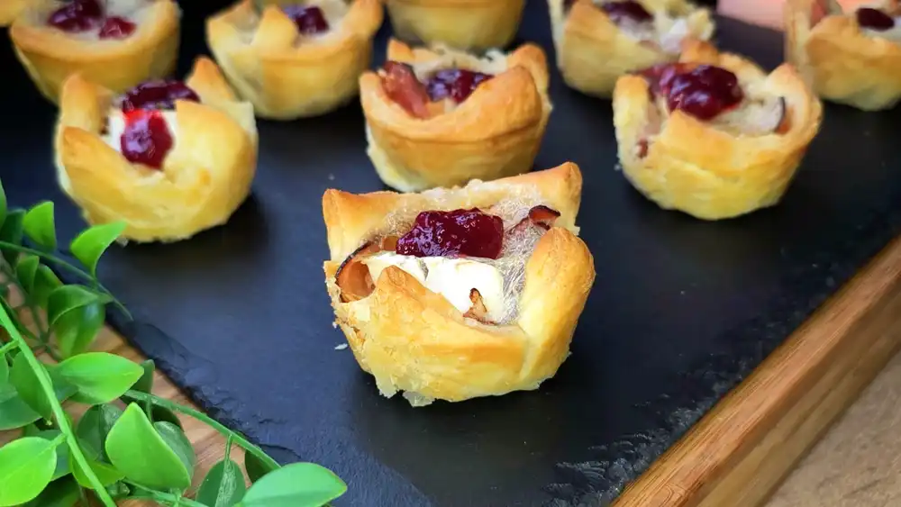 Goldbraun gebackene Blätterteig-Muffins mit Schinken, geschmolzenem Camembert und Preiselbeeren in einer Brotdose für den Schulstart.