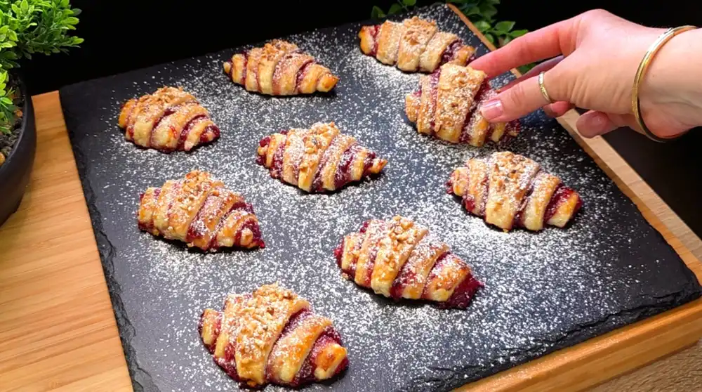 Goldbraun gebackene Blätterteig-Croissants gefüllt mit Johannisbeermarmelade, bestreut mit gehackten Haselnüssen und Puderzucker.