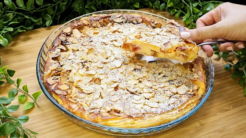 Goldbraun gebackener Blätterteig-Käsekuchen mit Zwetschgen, gehobelten Mandeln und Puderzucker bestäubt in einer 26-cm-Form.