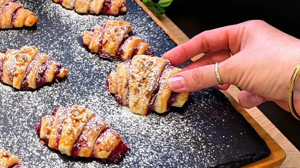 Detailansicht eines aufgeschnittenen Croissants mit Fokus auf die rote Johannisbeermarmelade, knackige Haselnüsse und den krossen Blätterteig.