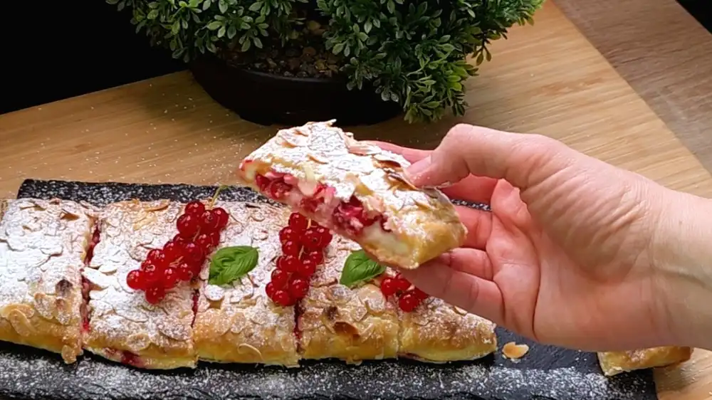 Detailansicht eines aufgeschnittenen Johannisbeer-Quark-Strudels mit Fokus auf die cremige Vanille-Quark-Füllung, saftige rote Beeren und die krossen Mandelsplitter.