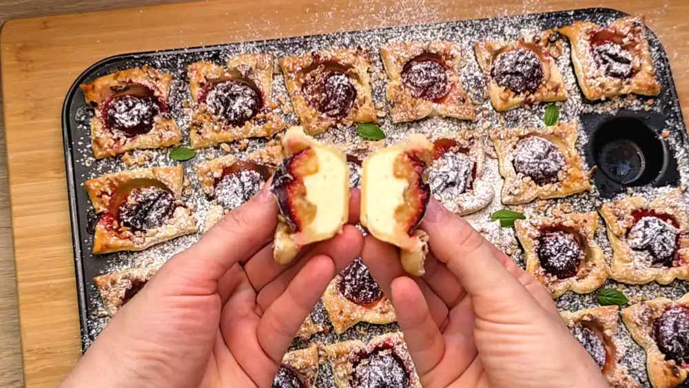 Detailansicht eines einzelnen Mini-Muffins mit Fokus auf die cremige Vanille-Quark-Füllung, die saftige Pflaumenhälfte und die krossen Haselnusskrümel.