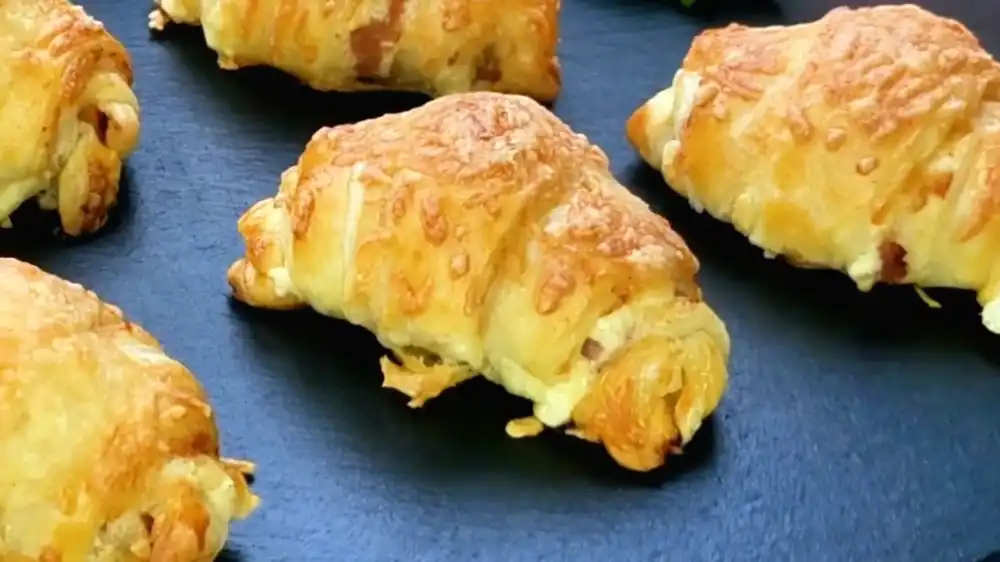 Detailansicht eines angeschnittenen Schinken-Käse-Croissants mit Fokus auf geschmolzenen Käse, Meersalz-Frischkäse und Prosciutto.