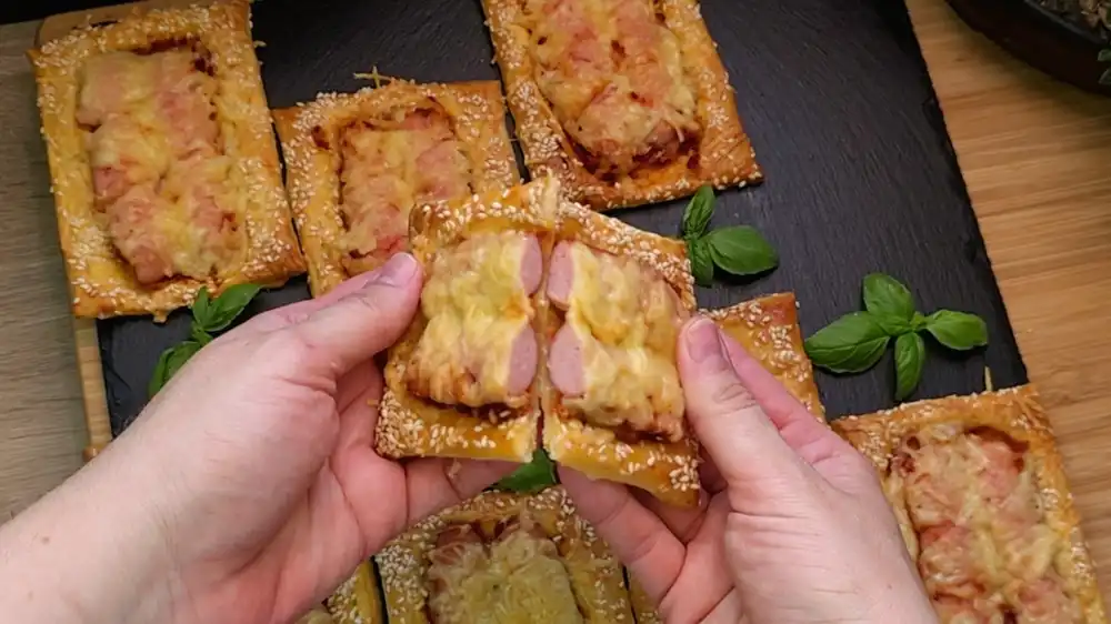 Detailansicht eines eingeritzten Würstchens im Blätterteig mit rotem Pesto und geschmolzenem Käse.