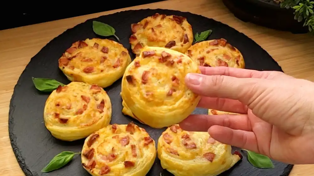 Detailansicht einer aufgerollten Blätterteigschnecke mit feinen Würstchen-Würfeln und geschmolzenem Käse.