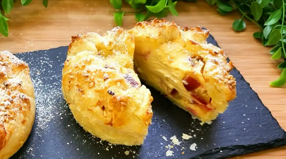 Detailansicht eines angeschnittenen Mini-Zwetschgen-Käsekuchens mit Fokus auf die cremige Käsekuchen-Füllung, saftige Zwetschgenwürfel und die krosse Haselnusskruste.