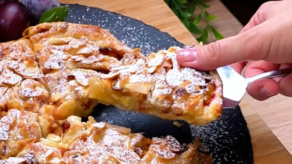 Detailansicht der kreisförmig gewickelten Blätterteig-Schnecke mit Fokus auf die cremige Vanille-Quark-Füllung, gebackene Zwetschgen und krosse Mandelplättchen.