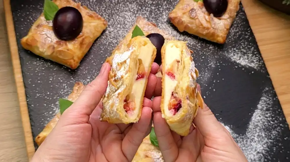 Detailansicht einer aufgeschnittenen Zwetschgen-Quark-Tasche mit Fokus auf die cremige Vanillequark-Füllung, saftige Zwetschgen und die Mandelkruste.