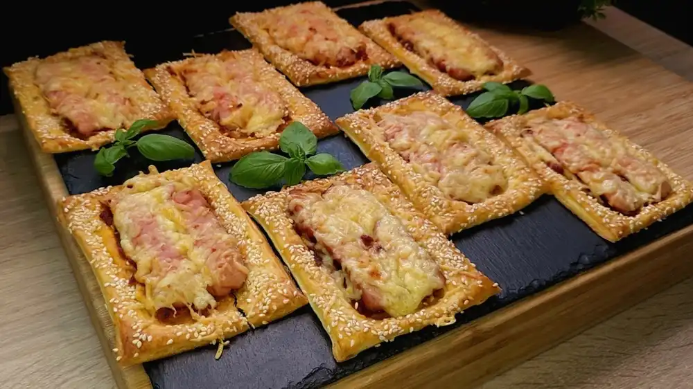 Goldbraun gebackene Würstchen auf Blätterteig mit rotem Pesto, geschmolzenem Käse und Sesam.