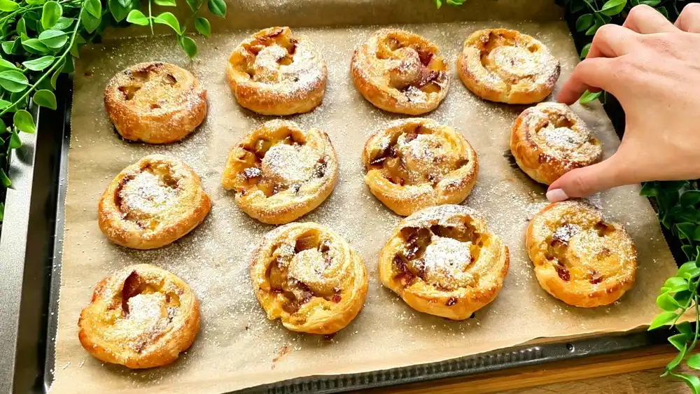 Goldbraun gebackene Zwetschgenschnecken aus Blätterteig mit Vanillepudding und Puderzucker.