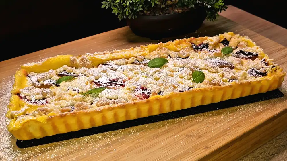 Goldbraun gebackener Blätterteig-Zwetschgen-Pudding-Streuselkuchen mit Puderzucker bestäubt auf einem Brett für den Schulstart.