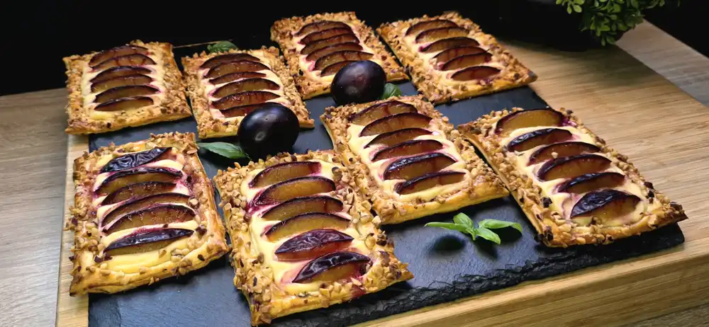Goldbraun gebackene Mini-Kuchen aus Blätterteig mit Quarkcreme, frischen Zwetschgenscheiben und gehackten Haselnüssen.