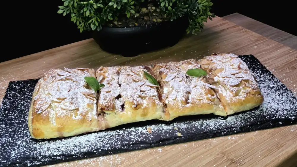 Goldbraun gebackener geflochtener Feigen-Quark-Strudel aus Blätterteig mit Mandeln und Puderzucker.