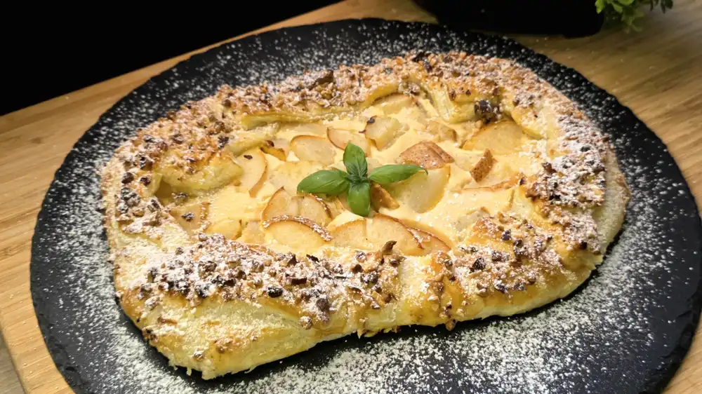 Goldbraun gebackene Galette aus Blätterteig gefüllt mit Vanille-Quark, Birnenstücken, gehackten Haselnüssen und Puderzucker.