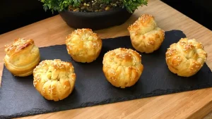 Goldbraun gebackene Knoblauch-Käse-Knoten aus Blätterteig in einer Muffinform mit Sesam.