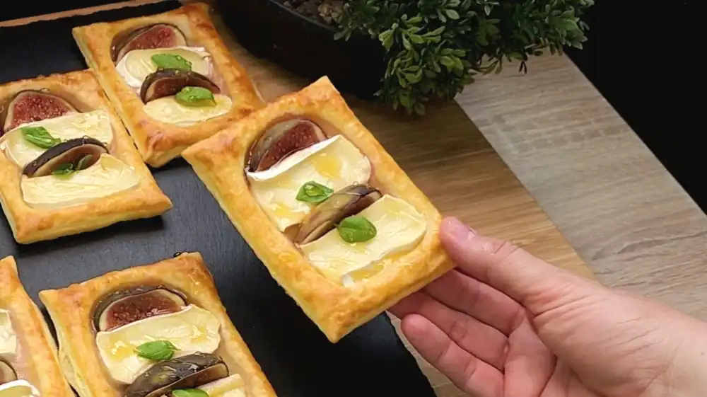 Detailansicht eines gebackenen Blätterteig-Teilchens mit zerlaufendem Camembert und saftiger Feige.