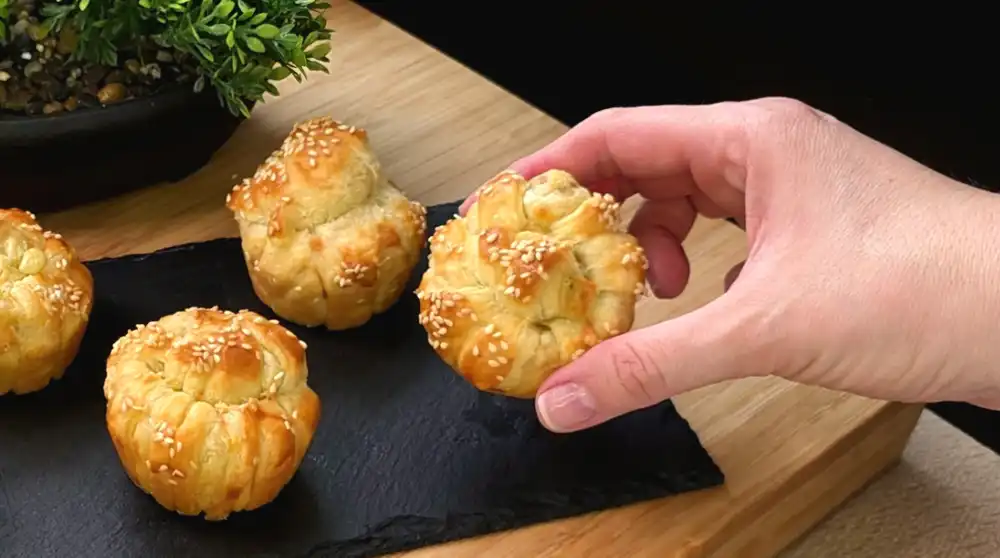 Detailansicht eines gebackenen Knoblauch-Käse-Knotens mit krossen Blätterteigschichten und geschmolzenem Käse.