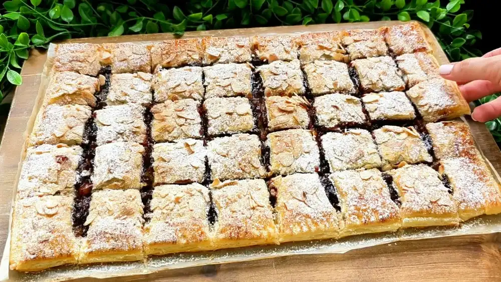 Goldbraun gebackener Zwetschgenkuchen aus Blätterteig mit gehobelten Mandeln und Puderzucker.